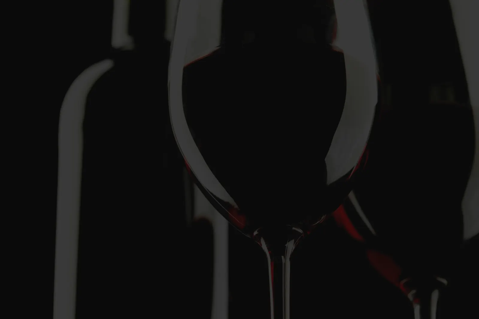 Copa y botella de vino tinto en penumbra